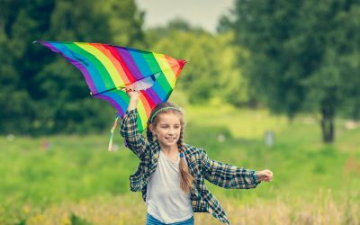 little cute girl flying a kite in a meadow on a sunny day